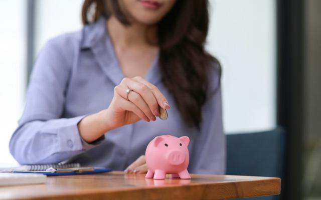 Weiterbildung für Beschäftigte: Ein rosafarbenes Sparschwein steht auf dem Tisch, in das eine langhaarige Frau eine Münze hineinsteckt.