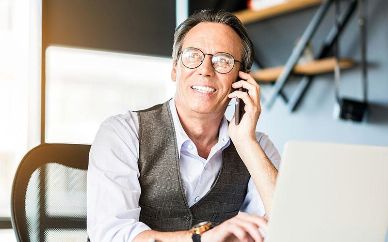 Nach dem Bildungsprämie-Ende telefoniert ein Herr mittleren Alters mit Brille am Schreibtisch, um sich über andere Förderungsmöglichkeiten zu informieren.