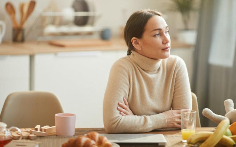 Kein Geld, keine Zeit: Junge Frau schaut nachdenklich und mit verschränkten Armen sitzend zur Seite, weil sie sich weiterbilden möchte, aber es nicht kann.