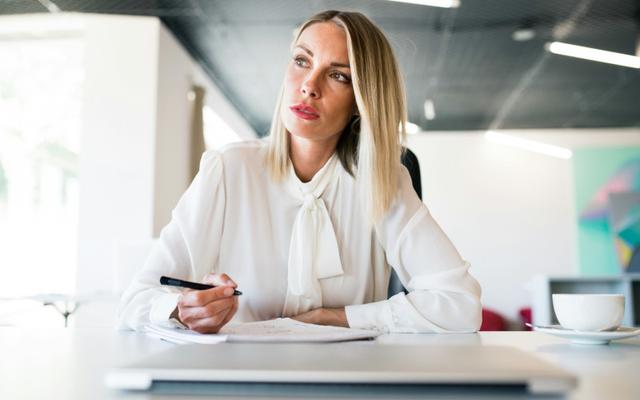 Weiterbildungsrepublik: Eine nachdenkliche junge, blonde Frau im Büro denkt über ihre Weiterbildungs- und Förderungsmöglichkeiten nach, während sie einen Stift in der Hand hält.