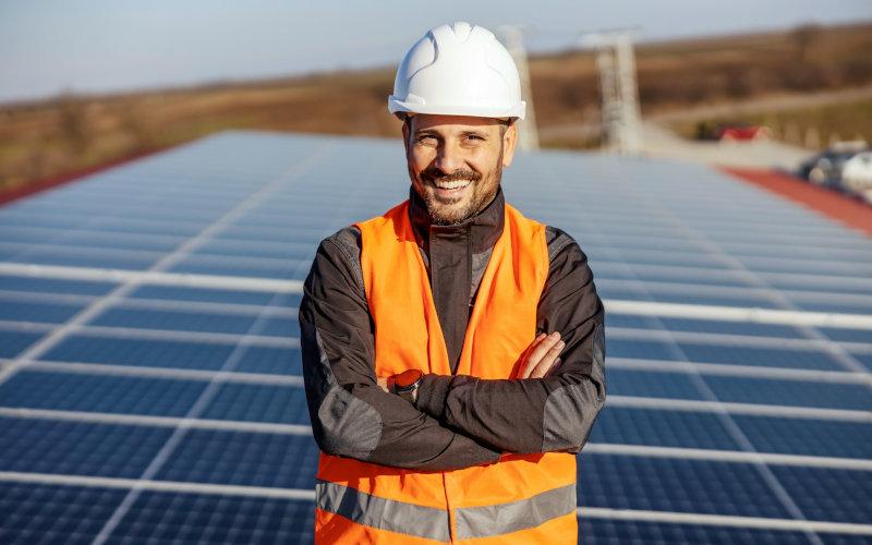 Grüne Jobs wie dieser lächelnde Handwerker, der vor Solarmodulen auf einem Dach steht, nehmen zu.